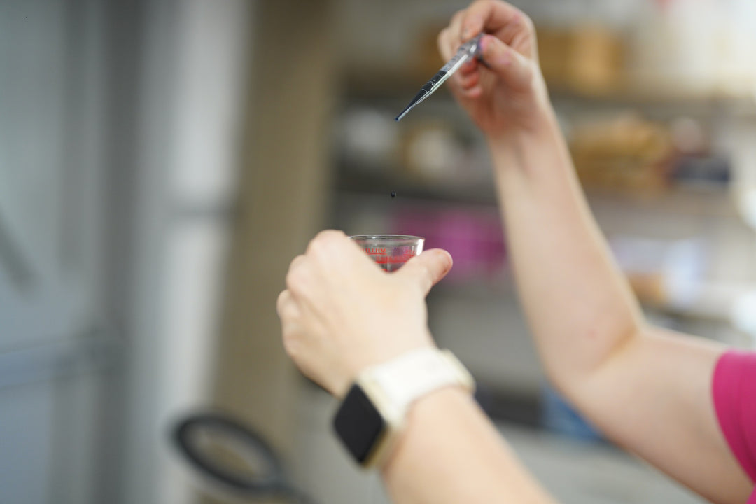 Person holding a spoon with a small amount of red liquid over a glass container.