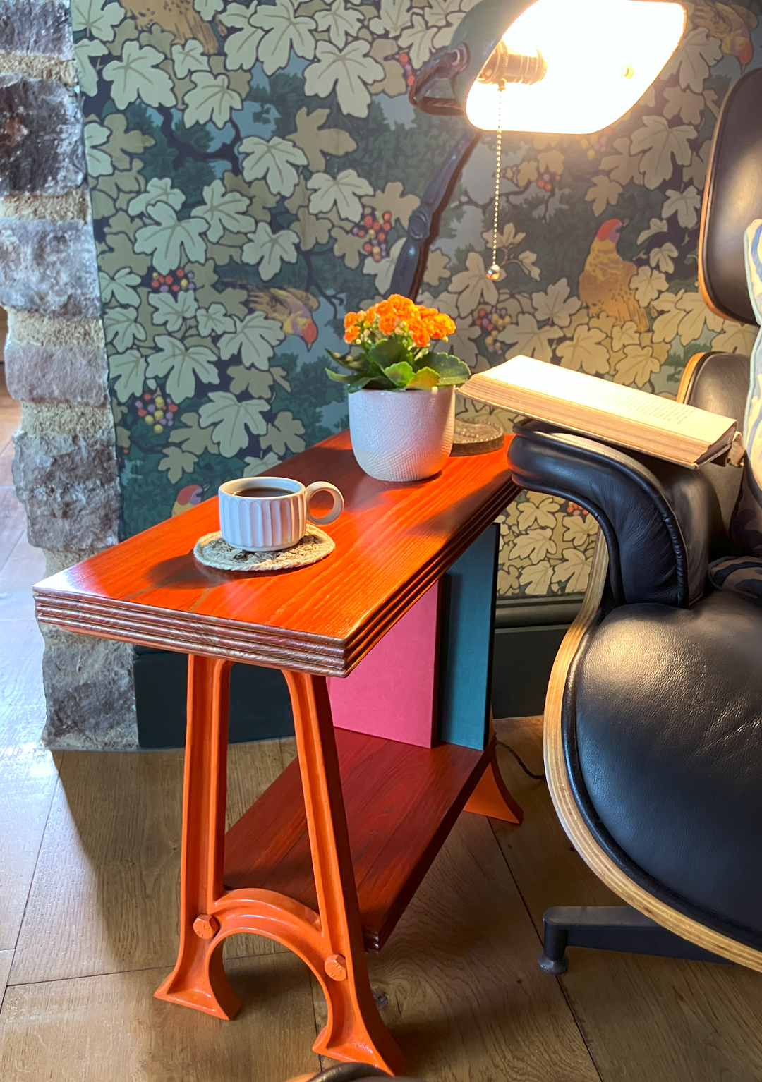 Orange Colpop table with gold grain in cosy reading corner, paired with Eames chair, small black coffee cup, lamp, and white pot with orange flower