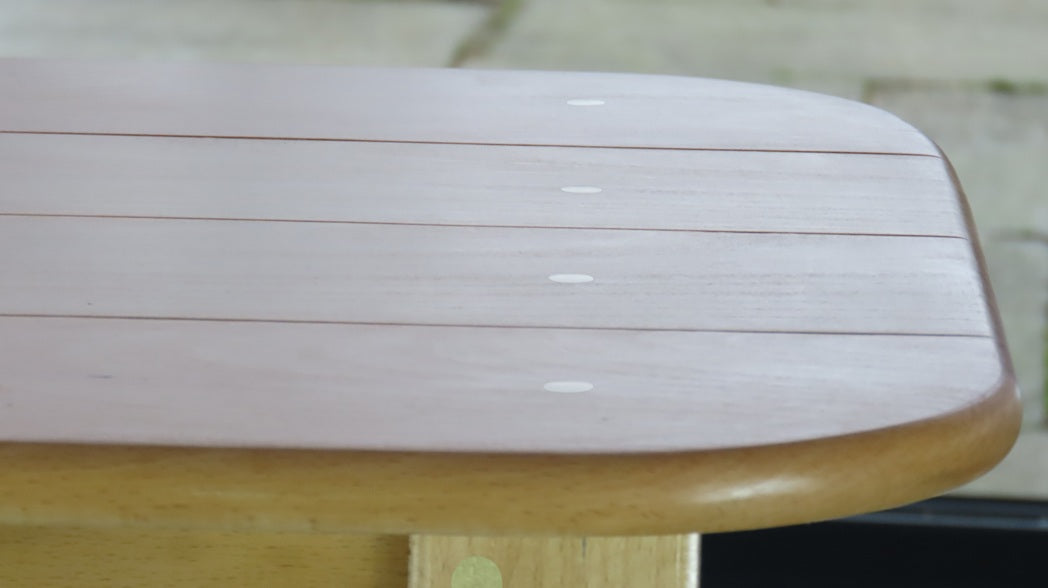 Close-up of tabletop with sunlight highlighting individual boards and solid brass dowels across the surface.