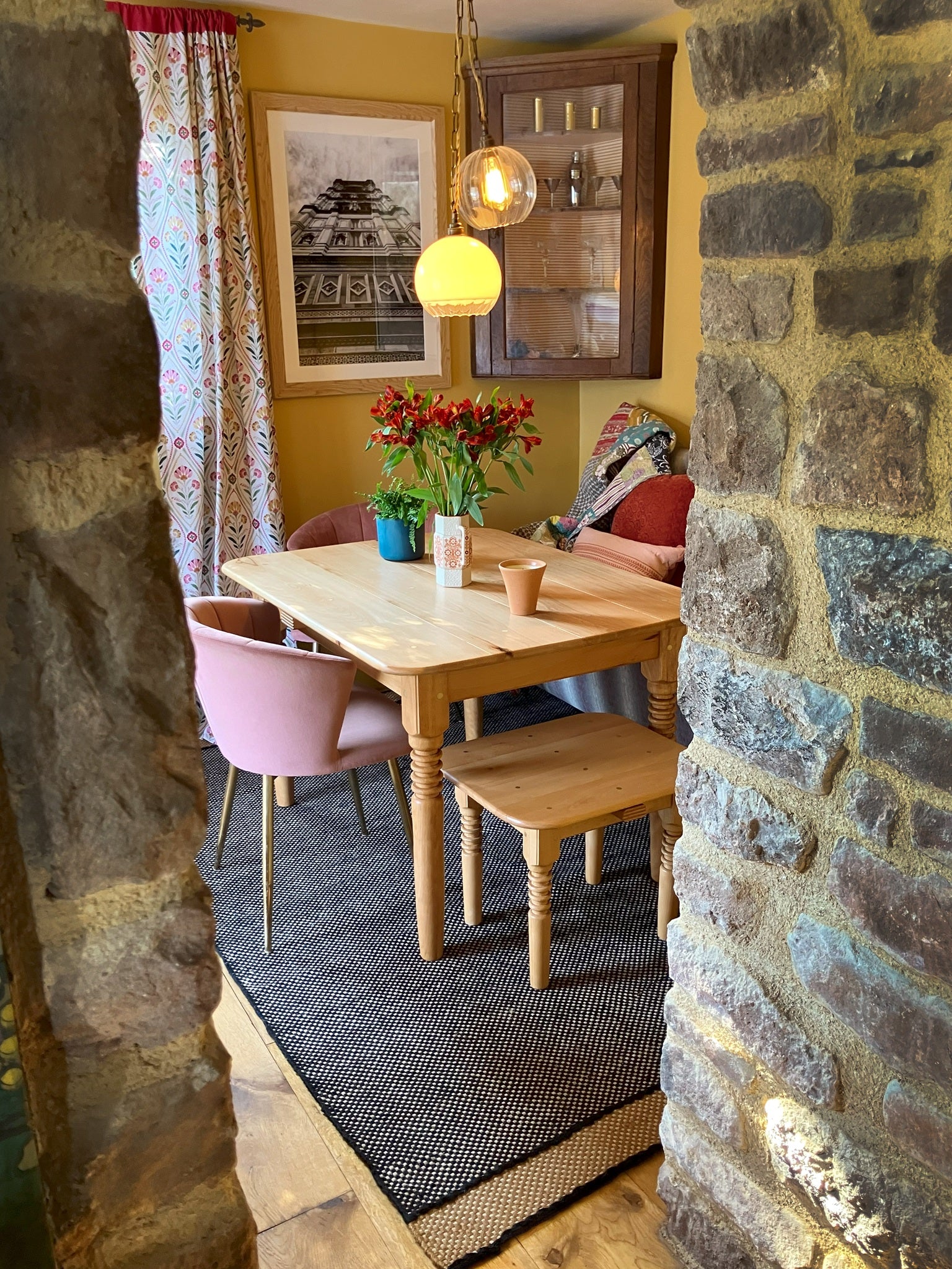 Farmhouse style wooden table and matching seat under warm pendant lights, framed by rustic stone archway, showcasing cozy vintage dining area with natural textures.