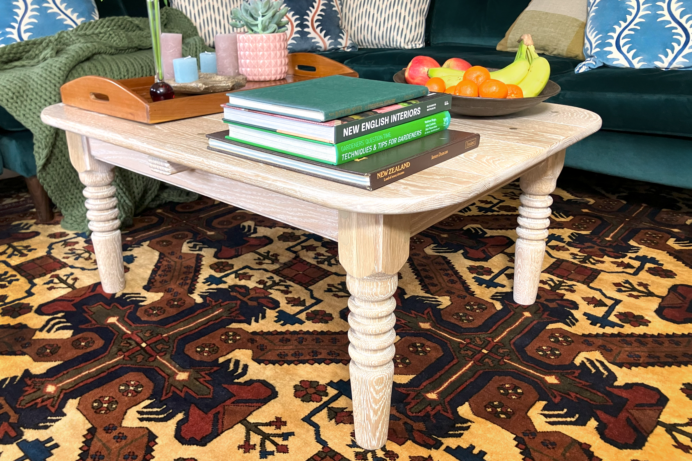 Lime-washed oak coffee table with unique turned legs and solid brass dowels, set on a Persian carpet in a rustic interior