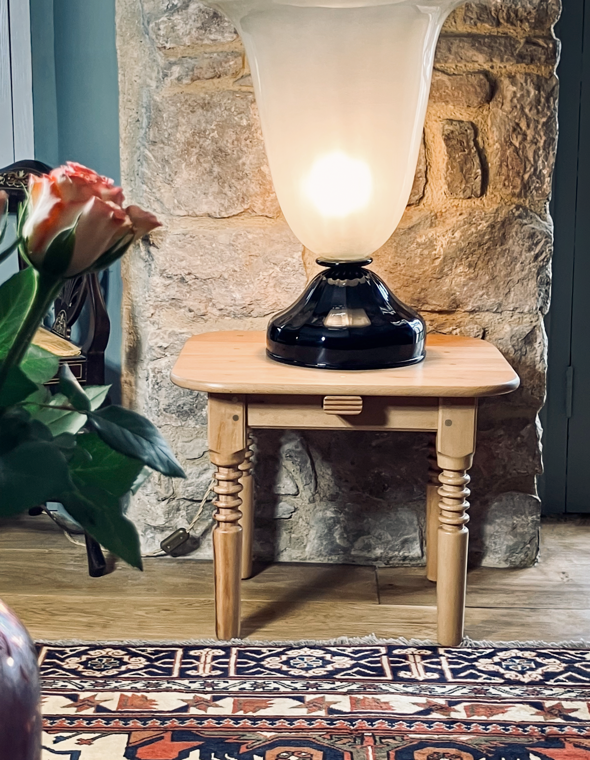 Handmade beech table with distinctive turned legs, beneath a large Art Deco light; roses softly blurred in the foreground.