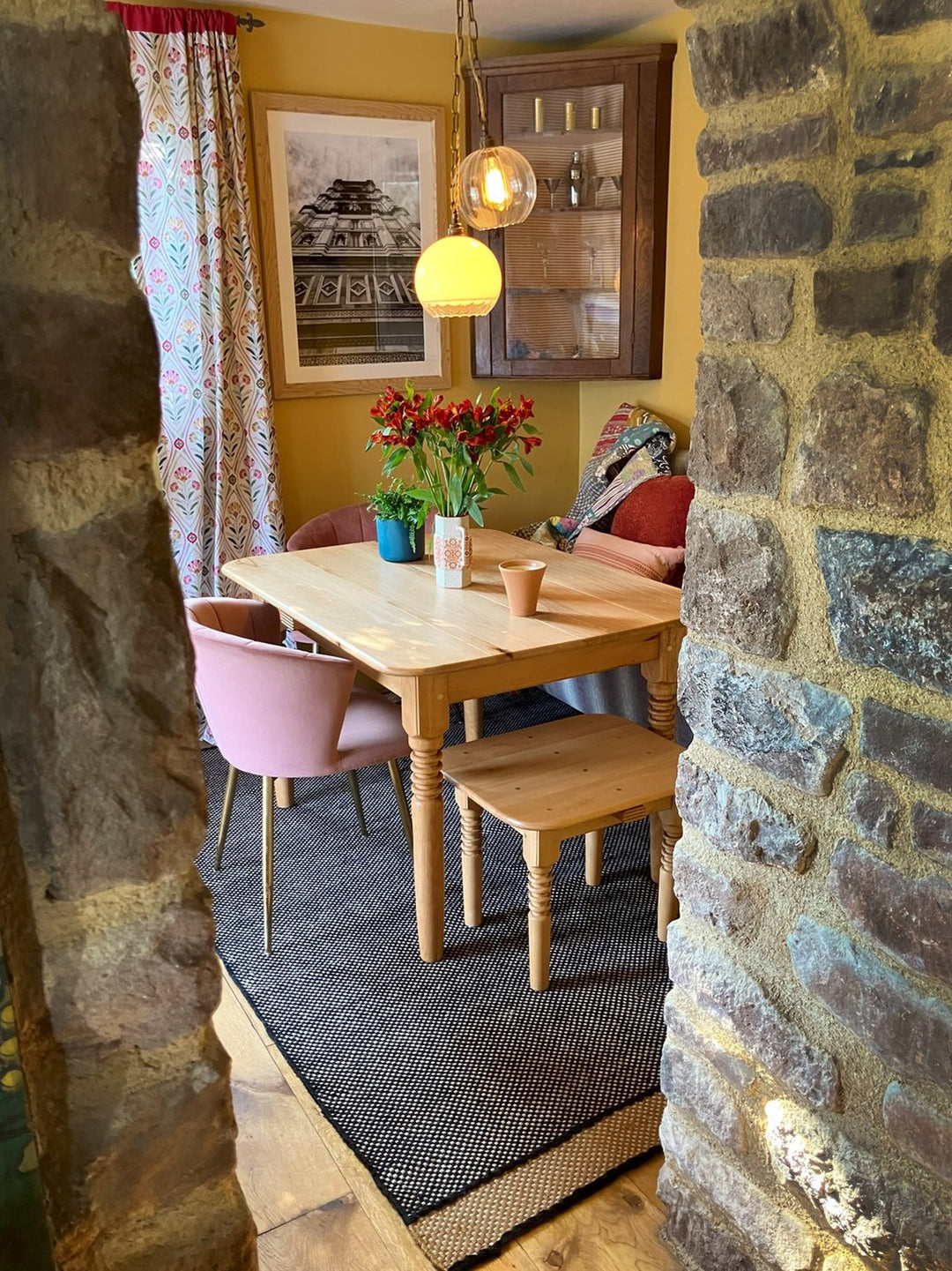 Farmhouse style wooden table and matching seat under warm pendant lights, framed by rustic stone archway, showcasing cozy vintage dining area with natural textures.